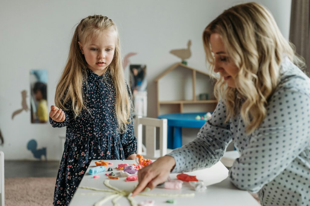 A young girl and a woman engage in a creative activity at a preschool classroom, fostering learning.